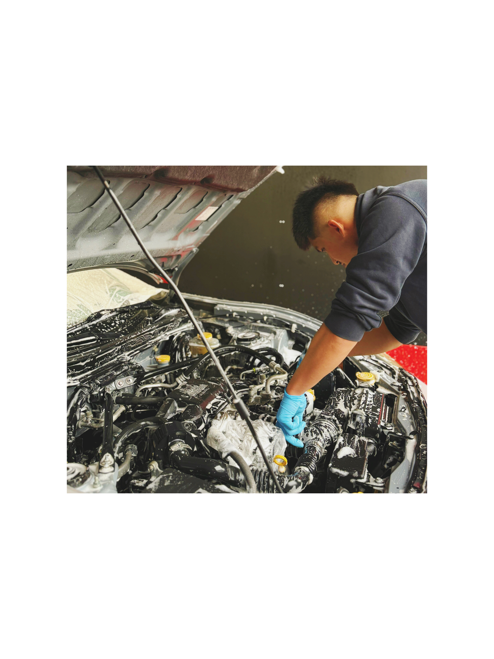 A detailer cleaning a foamed engine bay with a brush