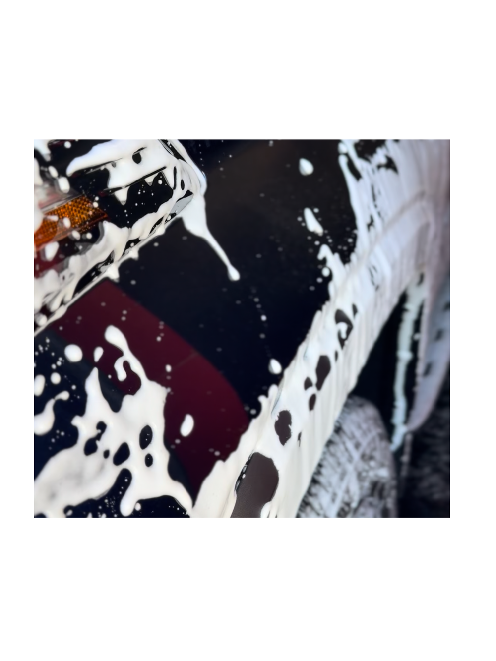A close-up of white wash foam across a dark vehicle panel