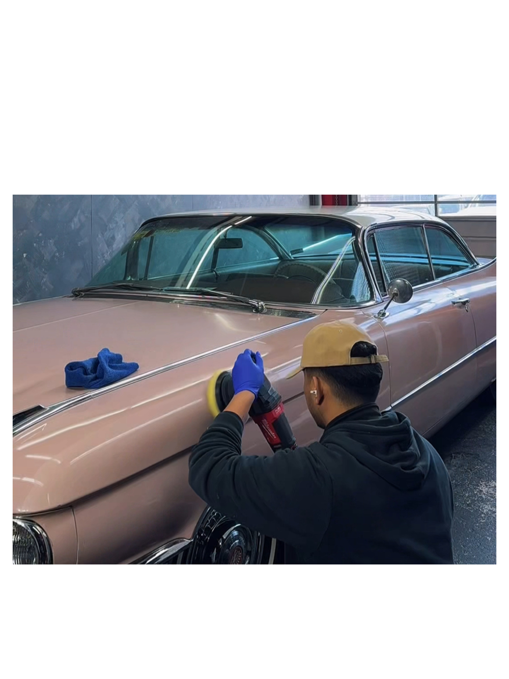 A detailer machine-polishing the front fender of a rose-coloured classic car